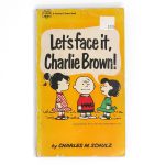 Front cover of the yellow vintage Fawcett Crest paperback book "Let's Face It, Charlie Brown!" by Charles M. Schulz, featuring Charlie Brown flanked by Patty and Lucy looking at him, with Charlie Brown in distress.