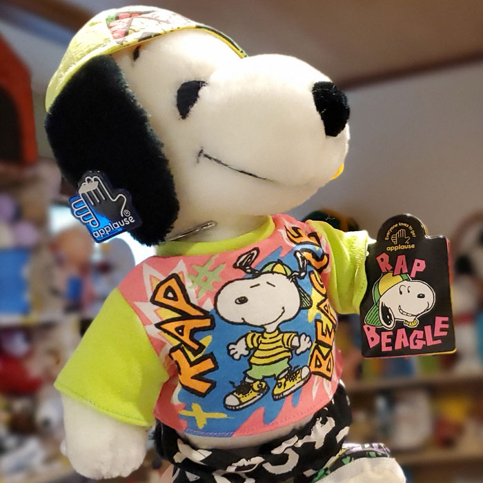 Rap Master Snoopy plush toy wearing a backwards yellow and green cap, neon rap graphic t-shirt, and pants with hanging tags from Applause