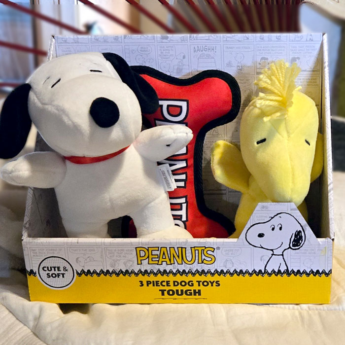 A Peanuts 3-piece dog toy set in its packaging, featuring a plush Snoopy doll, a yellow Woodstock doll, and a red bone-shaped toy with white text.
