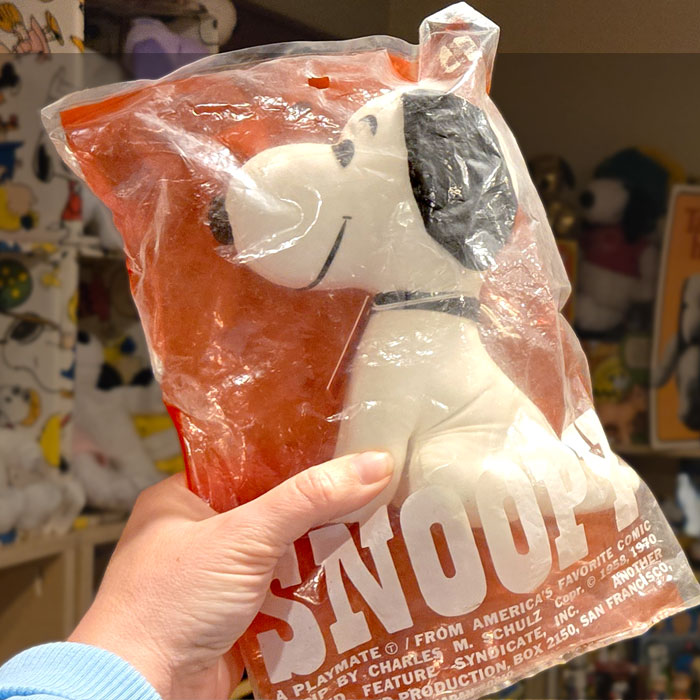A vintage Snoopy plush doll sealed in its original red and white plastic packaging with the "SNOOPY" logo and copyright text printed across the bottom.