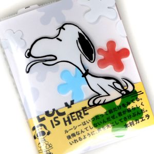 Lucy is Here! Snoopy Museum Exhibition book featuring an illustration of Snoopy with an orange flower and blue background elements against a white surface
