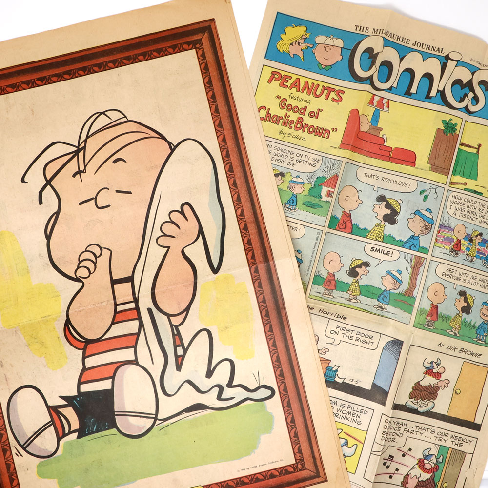 1968 Peanuts Newspaper Posters featuring an illustration of Charlie Brown sitting with Snoopy wrapped in a blanket, alongside a vintage Milwaukee Journal Sunday comics section.