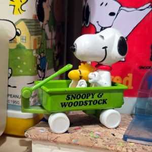 Close-up view of a green "Snoopy & Woodstock" pull wagon toy with white wheels and a yellow handle.