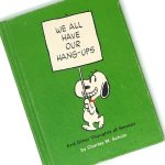 Green hardcover copy of We All Have Our Hang-Ups - Peanuts Hallmark Gift Book featuring Snoopy hanging from a sign that reads "WE ALL HAVE OUR HANG-UPS."