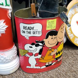 Vintage red Peanuts metal wastebasket featuring Snoopy as a director with a megaphone, Lucy, Charlie Brown, and a speech bubble reading "READY... ON THE SET!!" with a price tag attached.