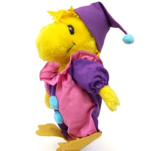 Plush Woodstock bird toy standing on a white background, dressed in a colorful clown costume featuring a pink ruffled collar, purple sleeves, pink pants with light blue pom-poms, and a purple jester cap with a light blue pom-pom on the tip.
