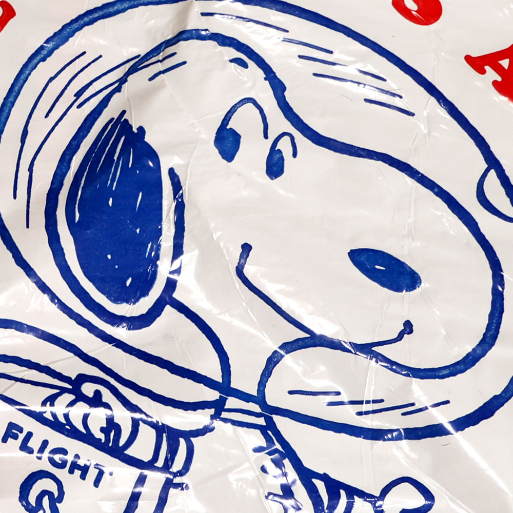 A close-up view of a vintage plastic kite featuring a blue line drawing of Snoopy as an astronaut, wearing a spacesuit helmet and collar that reads "FLIGHT".