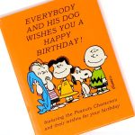 Orange hardcover copy of Everybody and their Dog Wishes You a Happy Birthday - Peanuts Gift Book featuring Charlie Brown, Snoopy, and other members of the Peanuts gang.