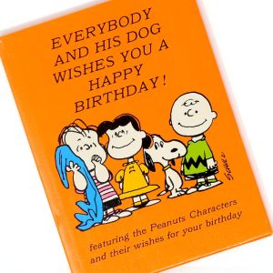 Orange hardcover copy of Everybody and their Dog Wishes You a Happy Birthday - Peanuts Gift Book featuring Charlie Brown, Snoopy, and other members of the Peanuts gang.