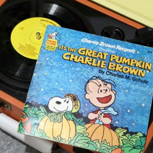 A vinyl record titled "It's the Great Pumpkin, Charlie Brown" playing on a record player, featuring the album cover artwork with Charlie Brown and Snoopy sitting amongst pumpkins.