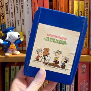 A blue 8-track tape featuring selections from the soundtrack to A Boy Named Charlie Brown with an illustration of Peanuts characters including Charlie Brown, Lucy, Linus, and Snoopy.