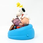 Hallmark Keepsake ornament featuring Charlie Brown reading a red book while sitting in a bright blue beanbag chair, with Snoopy lying on top of him and Woodstock perched on Snoopy's head.