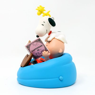 Hallmark Keepsake ornament featuring Charlie Brown reading a red book while sitting in a bright blue beanbag chair, with Snoopy lying on top of him and Woodstock perched on Snoopy's head.