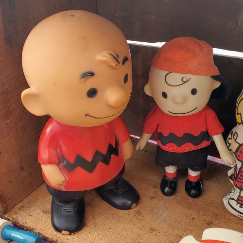 Vintage Hungerford Charlie Brown vinyl figurine standing next to a smaller Charlie Brown pocket doll wearing a red shirt with black zig-zag stripes and a matching red baseball cap.