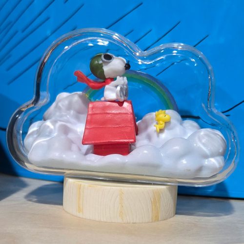 Snoopy wearing an aviator helmet and red scarf atop his red doghouse inside a cloud-shaped snow globe with Woodstock standing in the clouds.