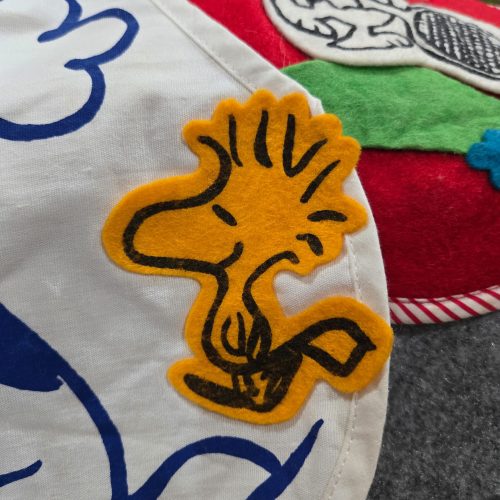 A close-up view of a yellow felt Woodstock patch stitched onto a white fabric Snoopy Bicentennial pajama bag, showing blue drawn details and stitched edges.