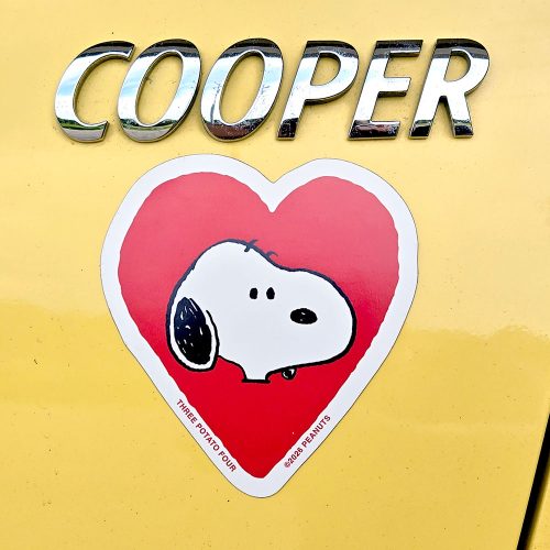 Snoopy heart sticker with the word "COOPER" in large metallic 3D bubble letters above a red heart-shaped sticker featuring Snoopy's face, with small text along the lower edge that reads "THREE POTATO FOUR" and copyright text for Peanuts