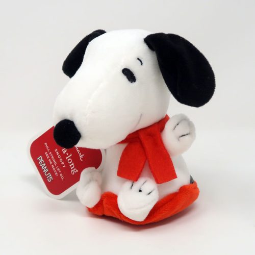 Snoopy Sled Zip-A-Long plush toy sitting and wearing a red scarf, with a round red product hang tag attached to its paw that reads "zip-a-long PEANUTS"